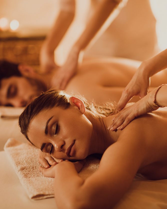 Two guests receiving side-by-side massages in a warmly lit room