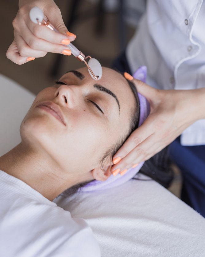 An esthetician working over a guest's face with a jade roller