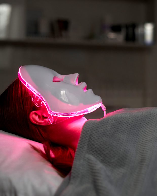 A guest wearing an illuminated red LED therapy mask